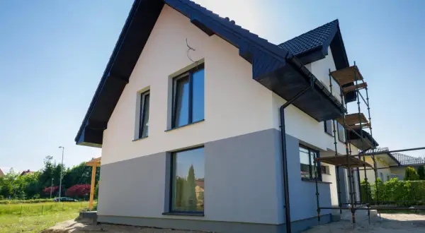 Nowy dom z dwukolorową elewacją, biało-szarą, czeka na malowanie elewacji domu wzory. Rusztowanie ułatwia pracę.