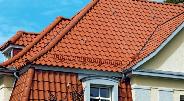 Czerwona dachówka kontrastuje z błękitem nieba. W oddali widać fragmenty białego dachu, który harmonijnie wtapia się w krajobraz.