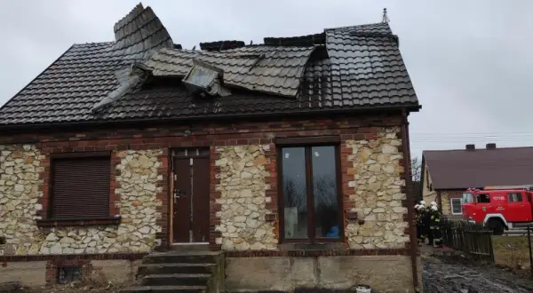 Zniszczony dach domu z kamienia wapiennego. Obok stoi wóz strażacki, a przy nim strażacy.