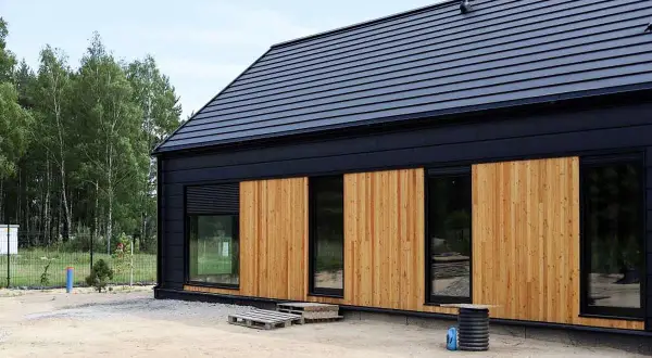 Nowoczesny modulo house z drewnianą elewacją i czarnym dachem, otoczony drzewami.