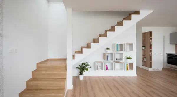 Nowoczesna klatka schodowa inspiracje: drewniane stopnie, białe ściany, geometryczne półki z książkami i roślinami.