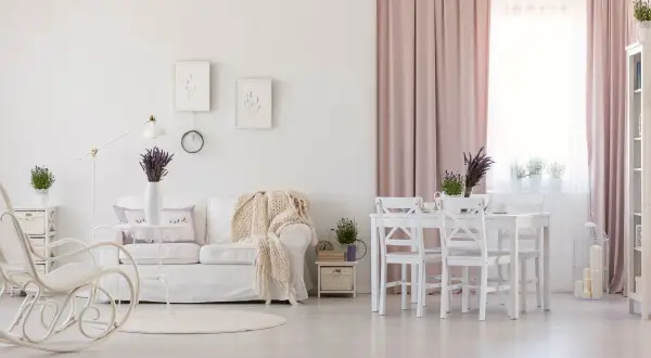 Jasny salon w stylu prowansalskim. Biała kanapa, fotel bujany, stół z krzesłami i lawenda tworzą przytulną atmosferę.