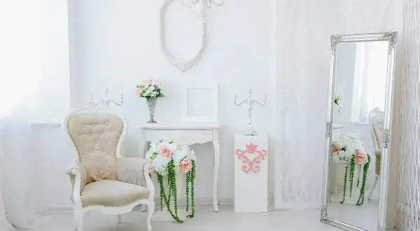 Eleganckie wnętrze w stylu shabby chic: kremowa sofa, lustro w ozdobnej ramie, świeczniki i bukiety kwiatów.