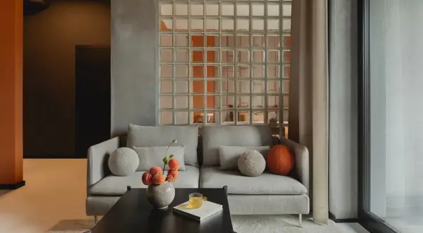 Nowoczesne luksfery aranżacje tworzą subtelny podział w salonie. Szara sofa z ozdobnymi poduszkami i wazonem z kwiatami.