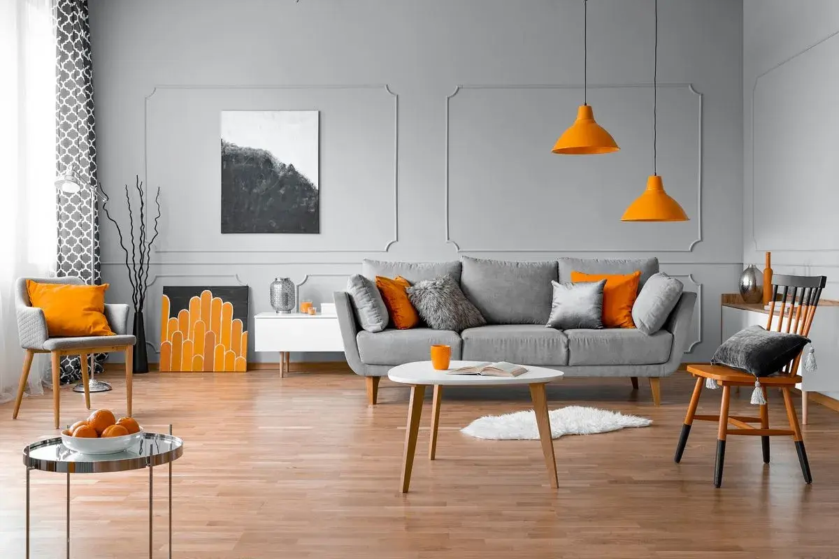 Nowoczesny salon z szarą kanapą, pomarańczowymi akcentami i sztukaterią ścienną inspiracje.