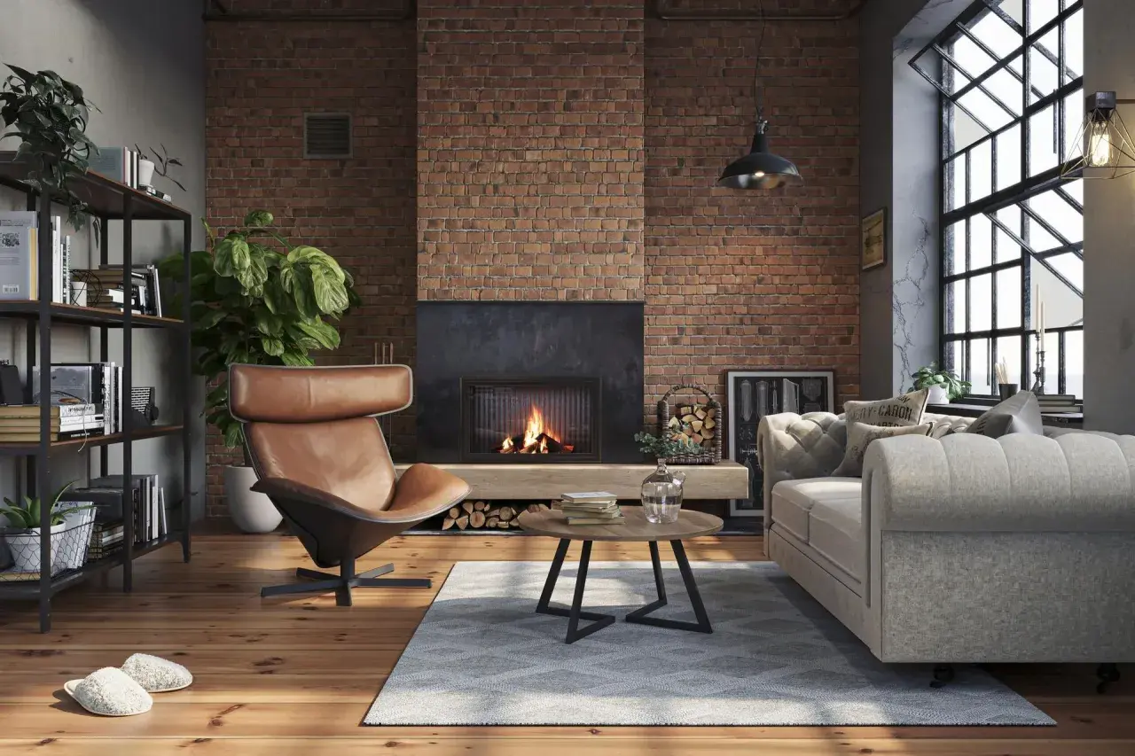 Przytulny, **soft loft** z palącym się kominkiem, skórzanym fotelem i szarą kanapą. Ceglana ściana i drewniana podłoga tworzą ciepłą atmosferę.