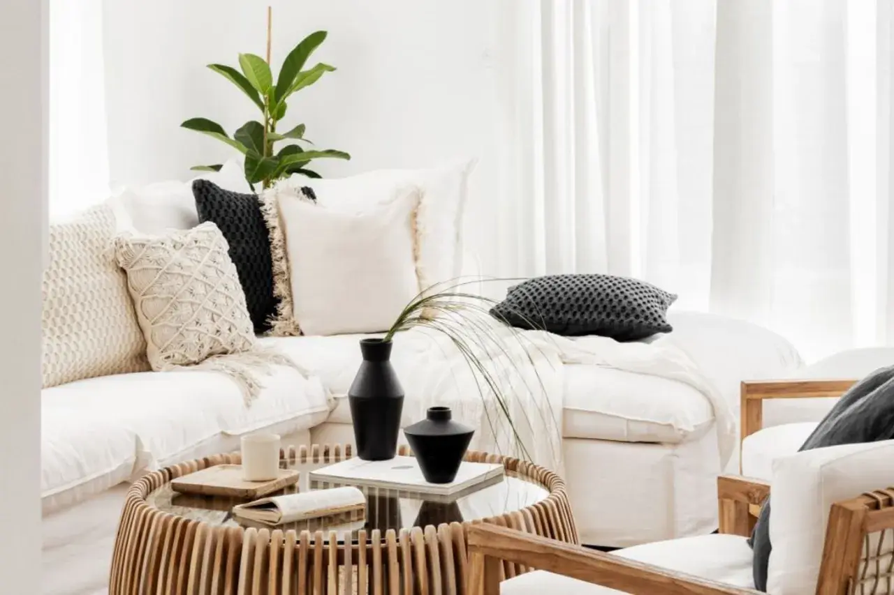 Przytulny salon w stylu boho: biała kanapa z poduszkami, stolik z rattanu, wazon i roślina.