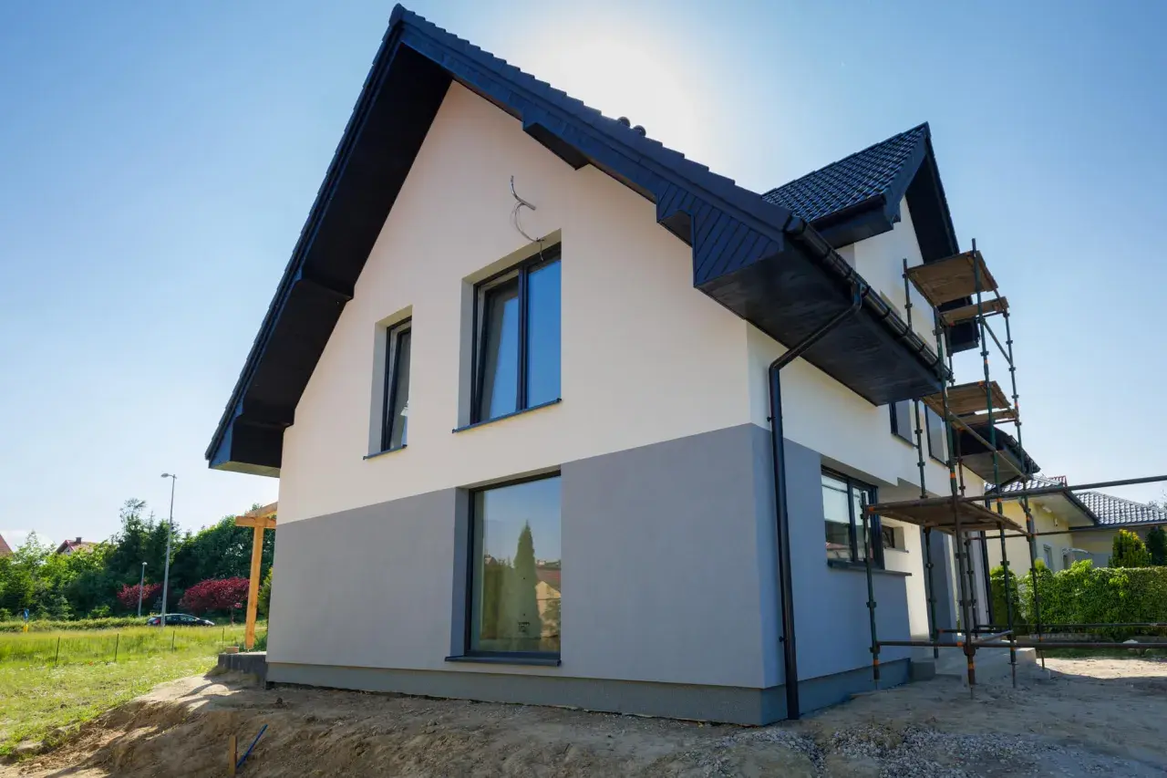 Nowy dom z dwukolorową elewacją, biało-szarą, czeka na malowanie elewacji domu wzory. Rusztowanie ułatwia pracę.
