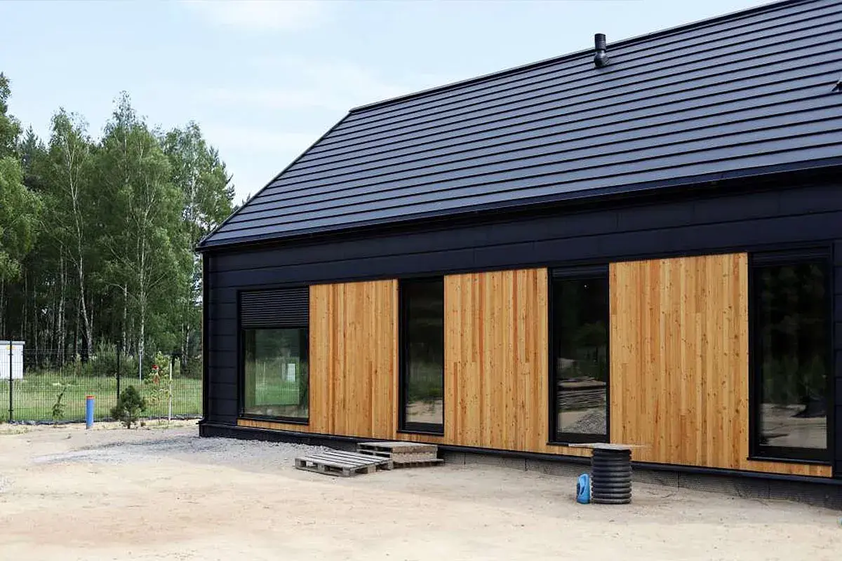 Nowoczesny modulo house z drewnianą elewacją i czarnym dachem, otoczony drzewami.