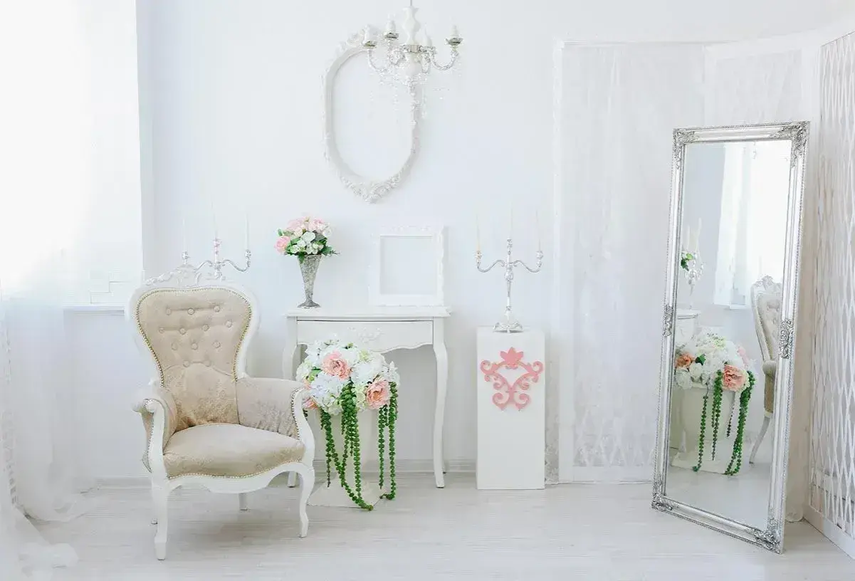 Eleganckie wnętrze w stylu shabby chic: kremowa sofa, lustro w ozdobnej ramie, świeczniki i bukiety kwiatów.