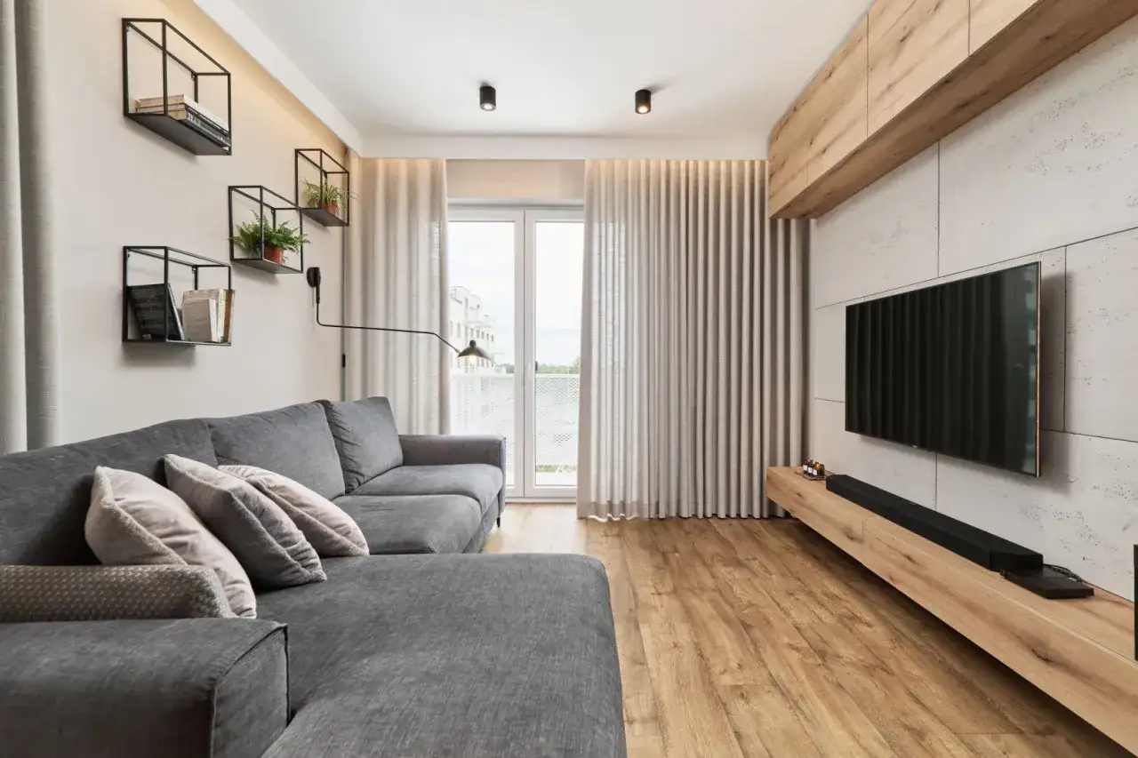 Nowoczesny salon z szarą kanapą, drewnianą podłogą i minimalistycznymi półkami. Mały pokój inspiracje dla miłośników stylu.