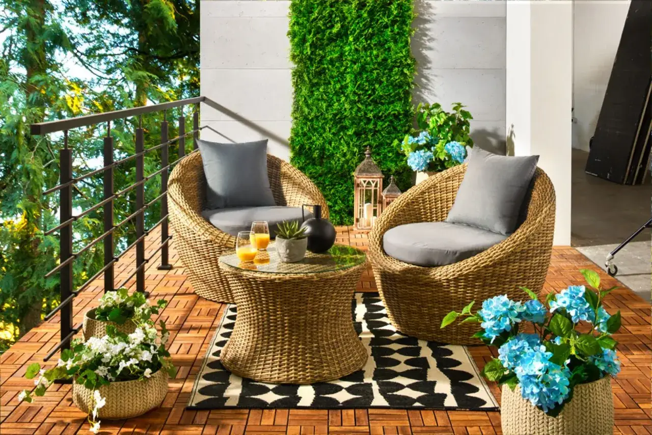 Wygodny zestaw mebli z rattanu na tarasie, z zieloną ścianą i kwiatami. Idealne balkon inspiracje na relaks.