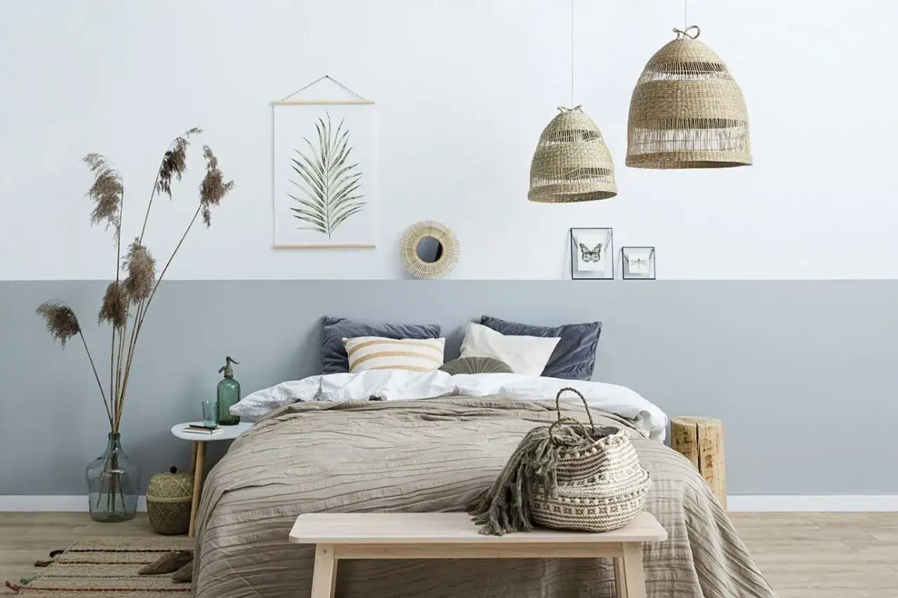 Sypialnia z łóżkiem i dwukolorową ścianą, pokazującą, jak połączyć dwa kolory na jednej ścianie. Wnętrze w stylu boho.