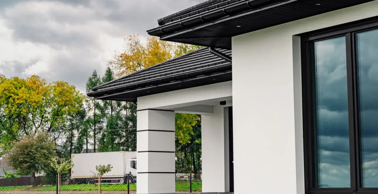 Nowoczesny dom z białymi ścianami i grafitowym dachem. Elegancka podbitka idealnie komponuje się z całością, tworząc spójną, stylową bryłę.