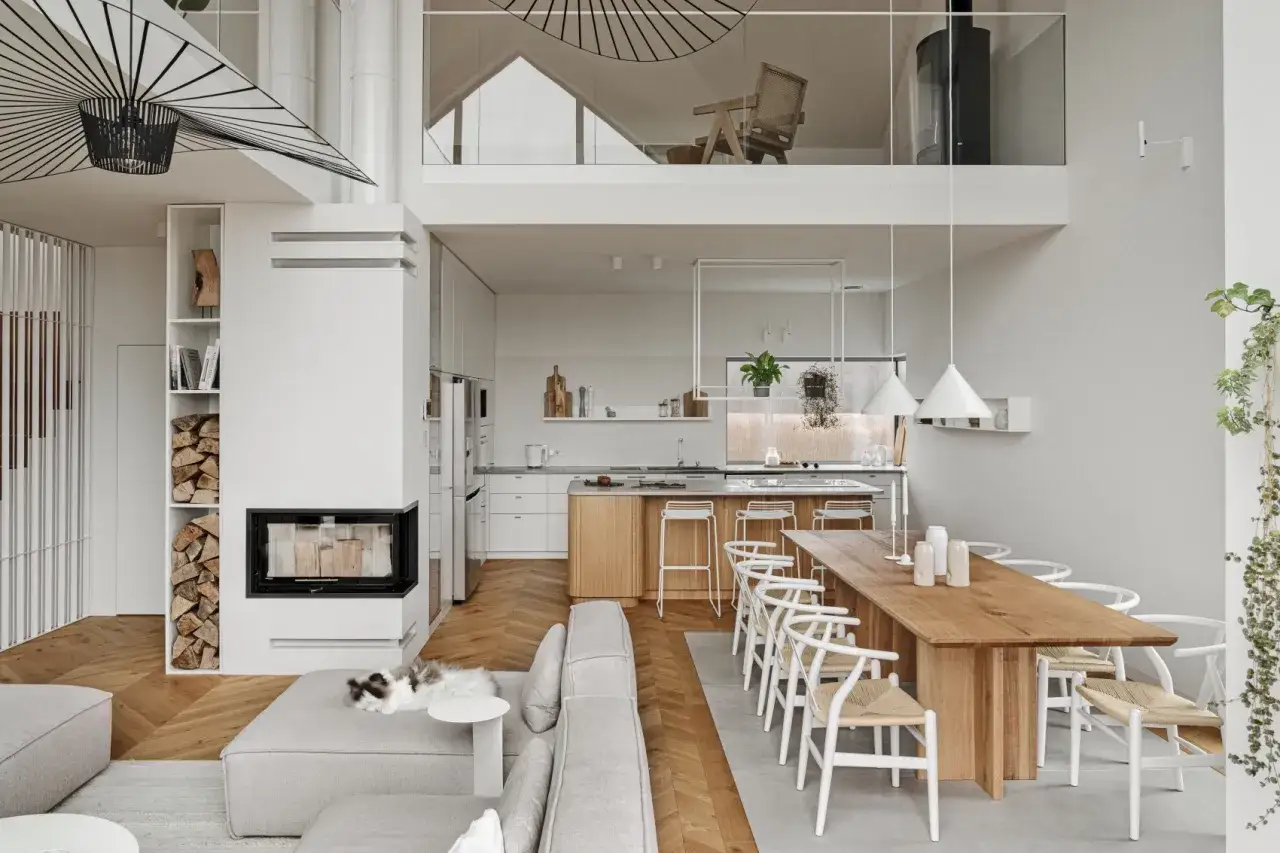 Jasny, przestronny dom w stylu modern farmhouse z kominkiem, drewnianą jadalnią i kuchnią. Kot odpoczywa na kanapie.
