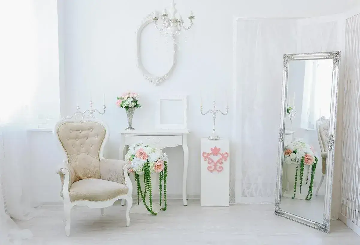 Jasny pokój w stylu shabby chic: kremowa sofa, wazon z kwiatami, lustro w ozdobnej ramie.