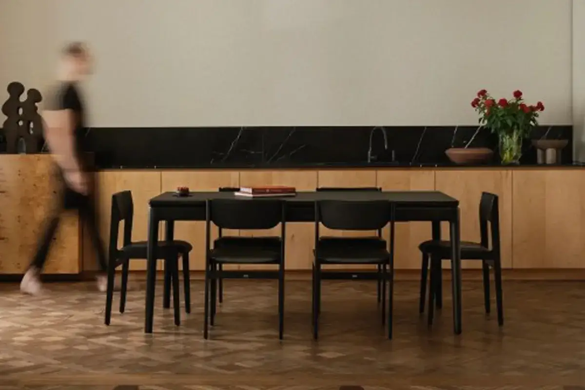 Elegancka jadalnia w stylu mid century modern z czarnym stołem i krzesłami, drewnianymi szafkami i bukietem czerwonych róż.