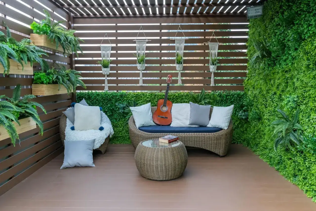 Zielony zakątek na balkonie w bloku: wiszące doniczki, sofa, fotel i gitara. Idealne miejsce, by osłonić balkon w bloku i stworzyć oazę spokoju.
