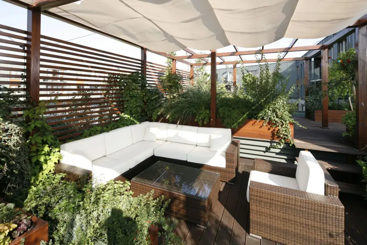 Taras w bloku inspiracje: biała sofa, rattanowe meble i mnóstwo zieleni tworzą oazę spokoju.
