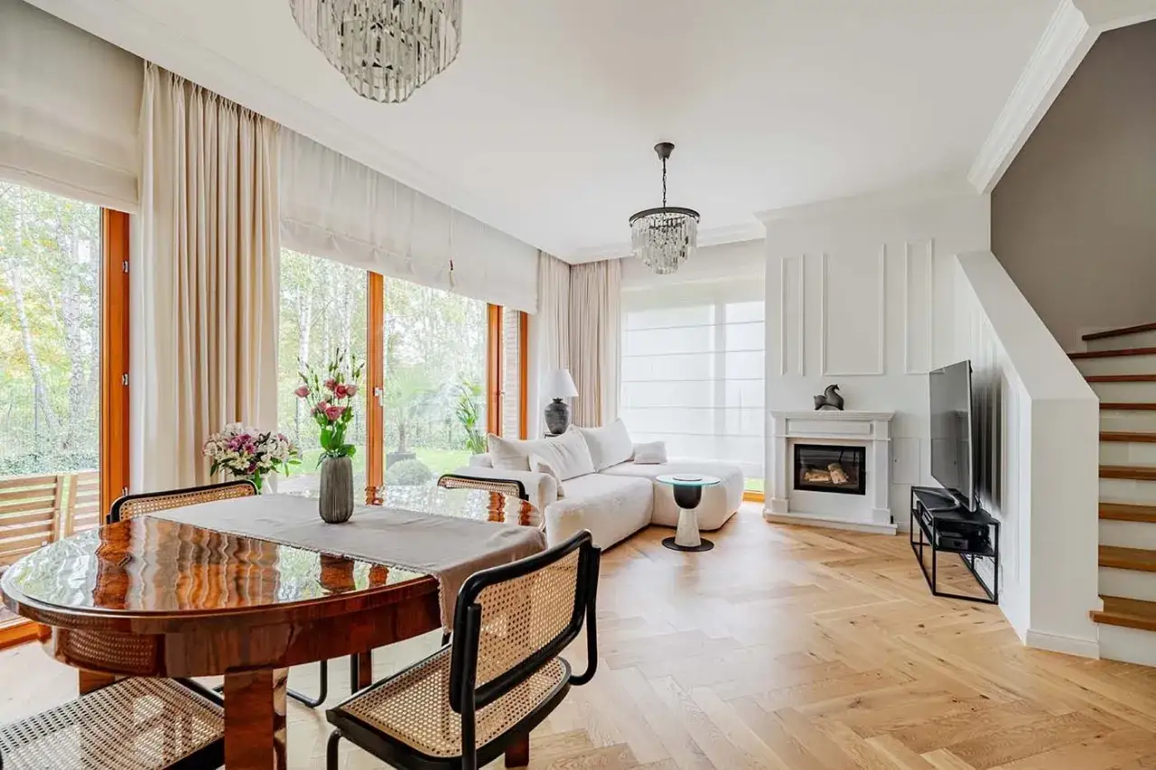 Elegancki salon z kominkiem i jadalnią, gdzie drewno i jasne tkaniny tworzą przytulny country glam.