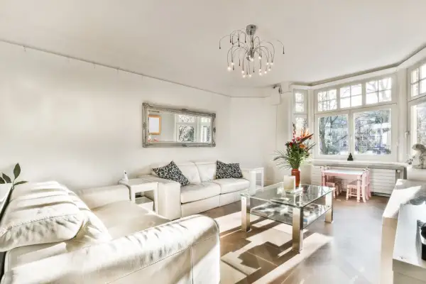 Jasny salon z białymi skórzanymi sofami, szklanym stolikiem i dużym oknem. Elegancki dom w stylu francuskim.