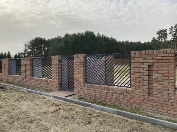 Solidne ogrodzenie z cegły z ozdobnymi metalowymi przęsłami, tworzące elegancką barierę przed lasem.