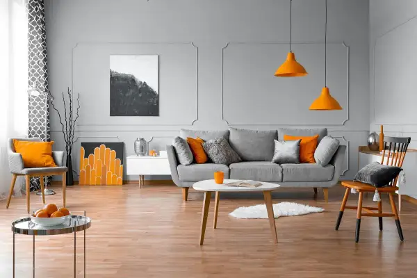 Nowoczesny salon z szarą kanapą, pomarańczowymi akcentami i sztukaterią ścienną inspiracje.