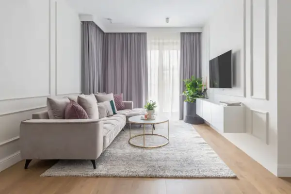 Elegancki salon w stylu modern classic. Jasna kanapa, okrągły stolik kawowy, dywan i zasłony tworzą przytulną atmosferę.