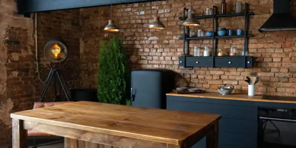 Drewniany stół i ceglana ściana tworzą przytulne loftowe wnętrza inspiracje. Widać lodówkę retro, industrialną lampę i wiszące lampy.