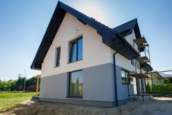 Nowy dom z dwukolorową elewacją, biało-szarą, czeka na malowanie elewacji domu wzory. Rusztowanie ułatwia pracę.