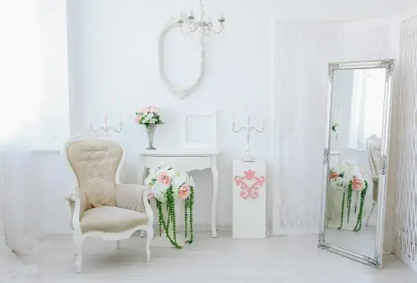Eleganckie wnętrze w stylu shabby chic: kremowa sofa, lustro w ozdobnej ramie, świeczniki i bukiety kwiatów.